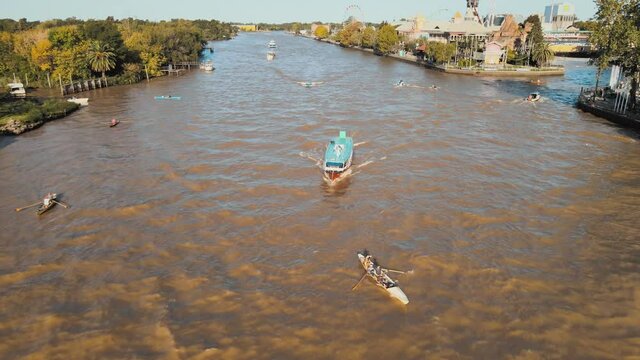 People Rowing Boat With Motorboat Tour Behind At Lujan River Near The Amusement Park At Tigre, Buenos Aires, Argentina. - aerial
