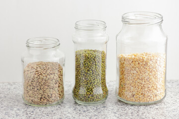 Variety of dry legumes: lentils, peas, green gram in glass jars uncooked on white kitchen background, zero waste, eco friendly, balanced diet food, healthy clean eating, vegan protein concept