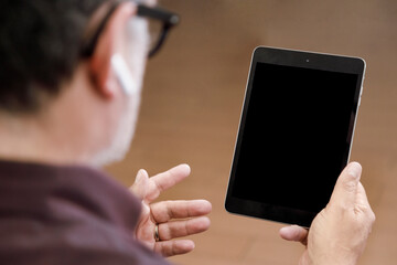 Un uomo tiene in. mano un tablet seduto a casa sua. Sullo sfondo si vede il pavimento