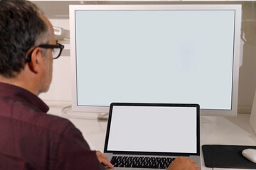 Dettaglio di un computer con schermo bianco davanti al quale un uomo lavora  seduto alla scrivania di u ufficio