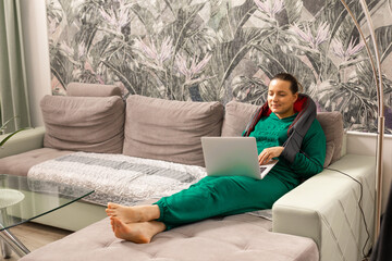 Electro massager and pillow for home or car massage on shoulders and neck of woman who receiving massage while working on laptop. Relaxing massage, home device health concept