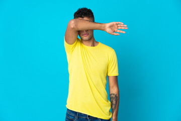Young Brazilian man isolated on blue background covering eyes by hands