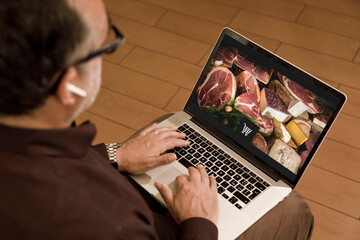 Un signore fa la spesa on-line da casa seduto davanti al suo computer portatile