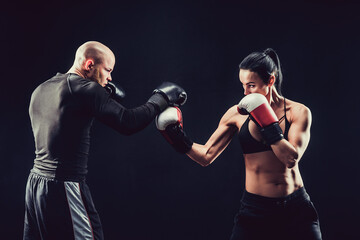 Shirtless Woman exercising with trainer at boxing and self defen