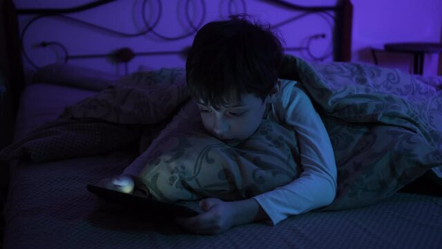 Schoolboy Laying In Bed Holding Cellphone, Watching Video Smartphone Addiction, Loneliness And Depression. Little boy Staring At Mobile Phone Screen At Night