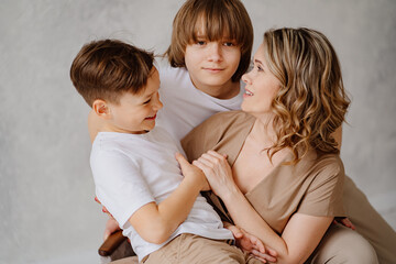 A mother and sons in beige and white clothes pose for a photo shoot