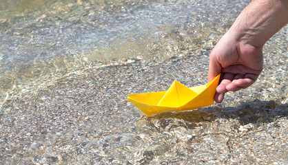 Hand holding origami paper boat on sea background