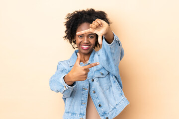 Young African American woman isolated on beige background focusing face. Framing symbol