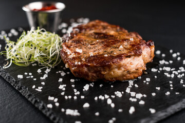 juicy chicken steak with red sauce and herbs on a stone textured plate and black background