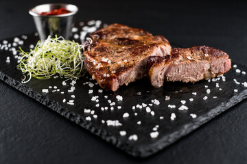 juicy chicken steak with red sauce and herbs on a stone textured plate and black background