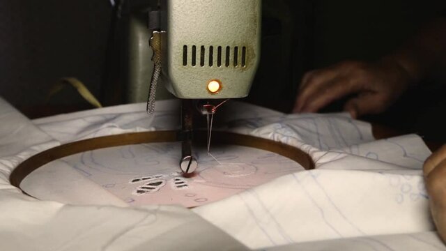 Wrinkled hands of a mature woman working on embroidery machine