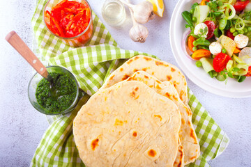 Homemade Indian naan flatbread with fresh salad and dips on the dinner table. Top view.