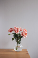 Pink rose in vase on wood table on gray wall background with copy space