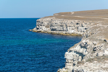 The sheer white cliffs of Cape Tarkhankut on the Crimean Peninsula rise above the waters of the Black Sea. Waves of dark blue, surprisingly rich color roll on the deserted beach of a secluded bay.