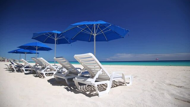 Beach calm scene with empty white sunbeds and blue sun umbrella near Caribbean sea. Tropical vacations