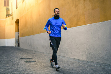 Male running and listening music during workout. Man run in the city and jogging alone. Runner with mobile phone connected to a smart watch recording data of sport activity with wearable technology.