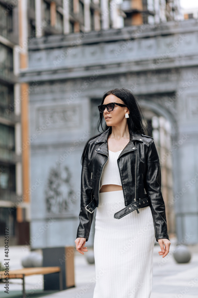 Wall mural Young beautiful brunette in sunglasses and a fashionable outfit walking in the city