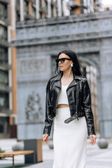 Fototapeta premium Young beautiful brunette in sunglasses and a fashionable outfit walking in the city