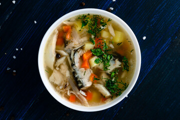 Hot tasty healthy soup with fish and vegetables served on a round plate on wooden table