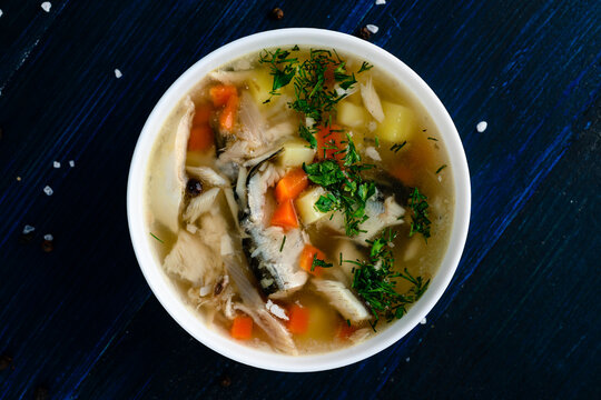 Hot tasty healthy soup with fish and vegetables served on a round plate on wooden table
