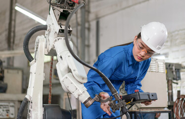 Female engineer checking robotic arm machine for system welding with remote control at a factory Industrial