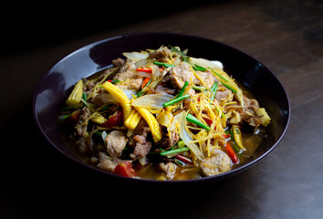 Stir fried pork and ginger with mixed vegetable in a black plate on wooden table