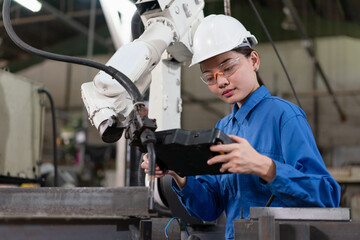 Female engineer checking robotic arm machine for system welding with remote control at a factory Industrial