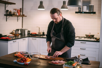 Fototapeta na wymiar A male chef prepares fresh meat at home in the kitchen..