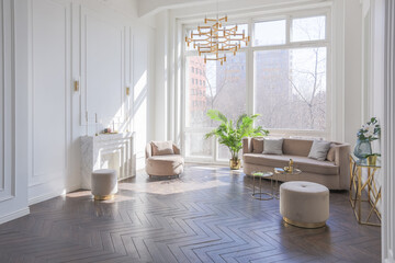 very light and bright interior of luxurious cozy living room with chic soft beige furniture with gold metallic elements, huge window to the floor and wooden parquet