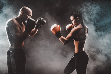 Shirtless Woman exercising with trainer at boxing and self defen
