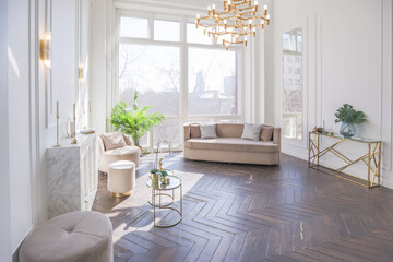 Fototapeta premium very light and bright interior of luxurious cozy living room with chic soft beige furniture with gold metallic elements, huge window to the floor and wooden parquet
