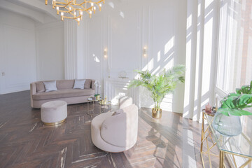 very light and bright interior of luxurious cozy living room with chic soft beige furniture with gold metallic elements, huge window to the floor and wooden parquet