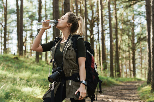 Female Hiker Drinking Water From Reusable Bottle In Green Forest