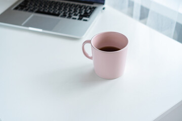 there is a pink mug and a laptop on the table