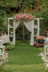 Wedding arch made of cloth and white and pink flowers on a green natural background. Old doors, rustic style