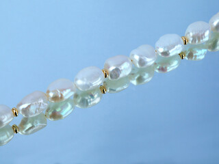 Line of baroque pearls on light blue mirror background