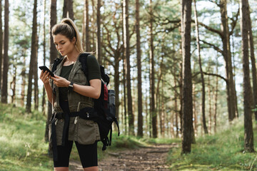 Female hiker is using smartphone for navigation in green forest