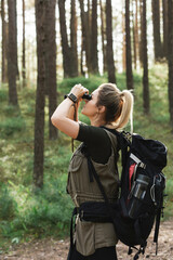 Female hiker is using binoculars for bird watching in green forest