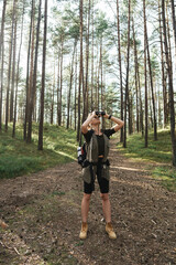 Female hiker is using binoculars for bird watching in green forest