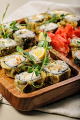 Close-up assorted hot rolls with eel, Japanese omelet, cream cheese, fried onions and unagi sauce with fresh herbs. Japanese food on a bamboo platter. Vertical shot