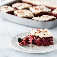 Close up of a red velvet chocolate square with a fork full on a plate and a pan of more squares in behind.