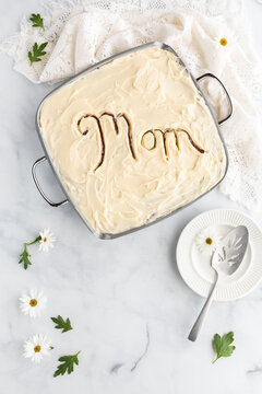 Top down view of a cream cheese frosted cake with 'Mom' carved into the top, ready for serving. Mother's Day concept.