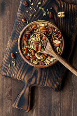 Top down view of a bowl of trail mix on a wooden board with a wooden spoon scooping some out.