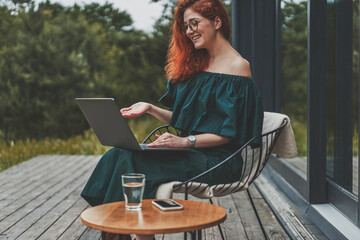 Side view of happy woman working with laptop and sitting outdoor in a beautiful terrace
