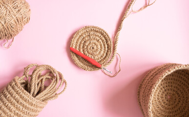 The knitted part of the basket made of jute rope and a crochet hook on a beige background. Hobbies, needlework, organization of space.