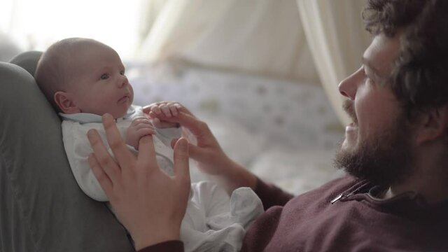 Crop father playing and talking to newborn baby at home