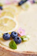 cheesecake with lemon and blueberries decorated with flowers on a wooden base on a light background