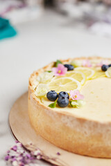 cheesecake with lemon and blueberries decorated with flowers on a wooden base on a light background