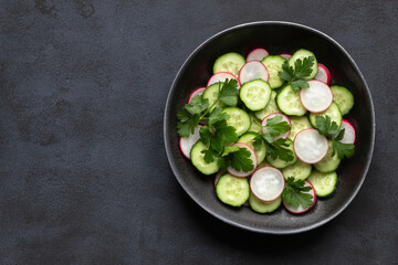Cucumber and radish fresh salad in plate on black background. Concept summer, spring, diet, vegan menu