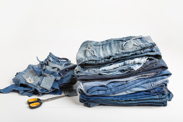 Upcycle old denim garbage. Recycling old jeans. Stack of old blue jeans, cut pieces ready for recycling and scissors on white background. Circular economy. Pile of discarded old blue jeans. Zero waste
